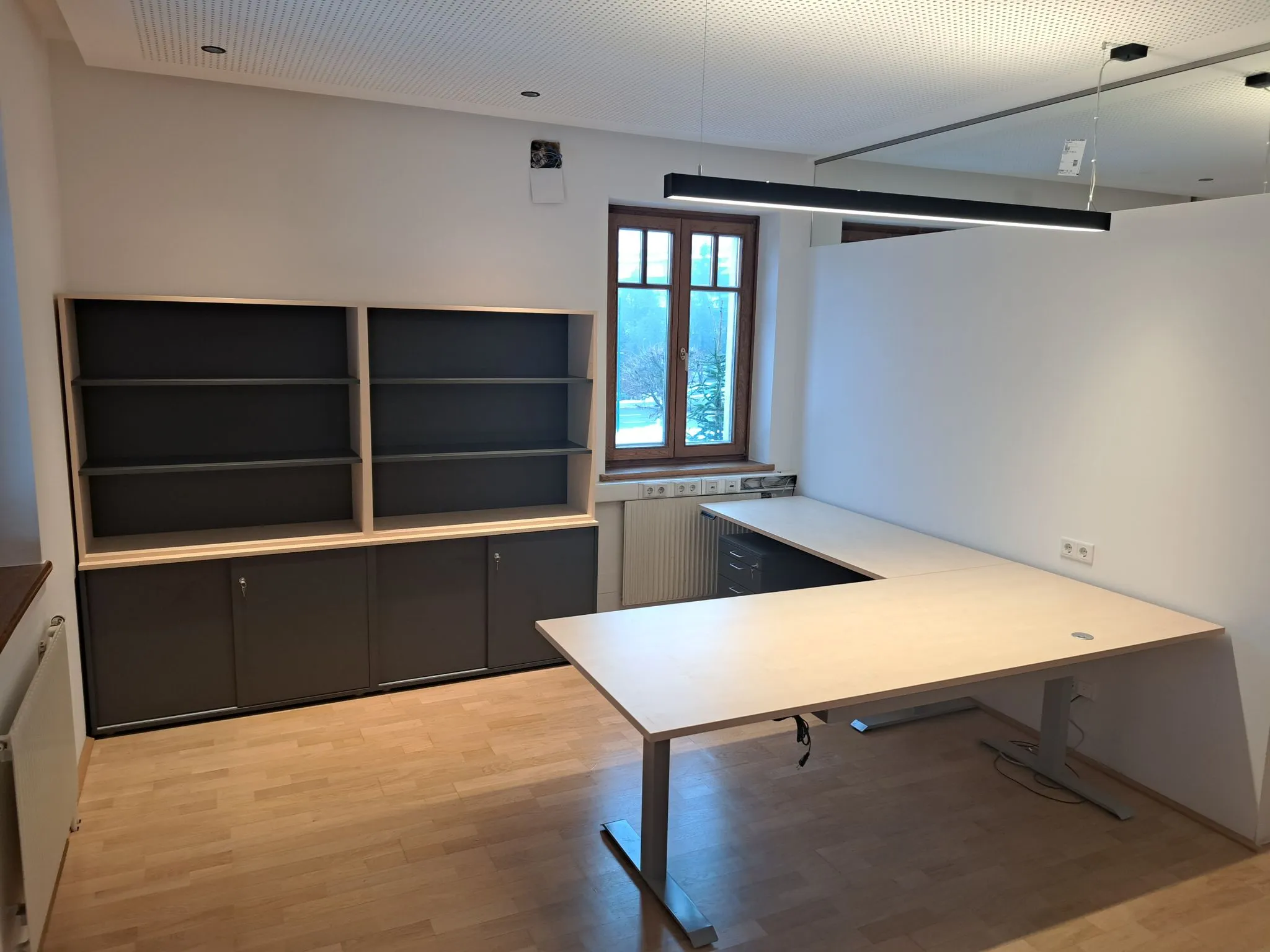 Leerer moderner Büroarbeitsplatz mit hellem Holz-Schreibtisch, grauem Regal und Fenster mit Holzkante.