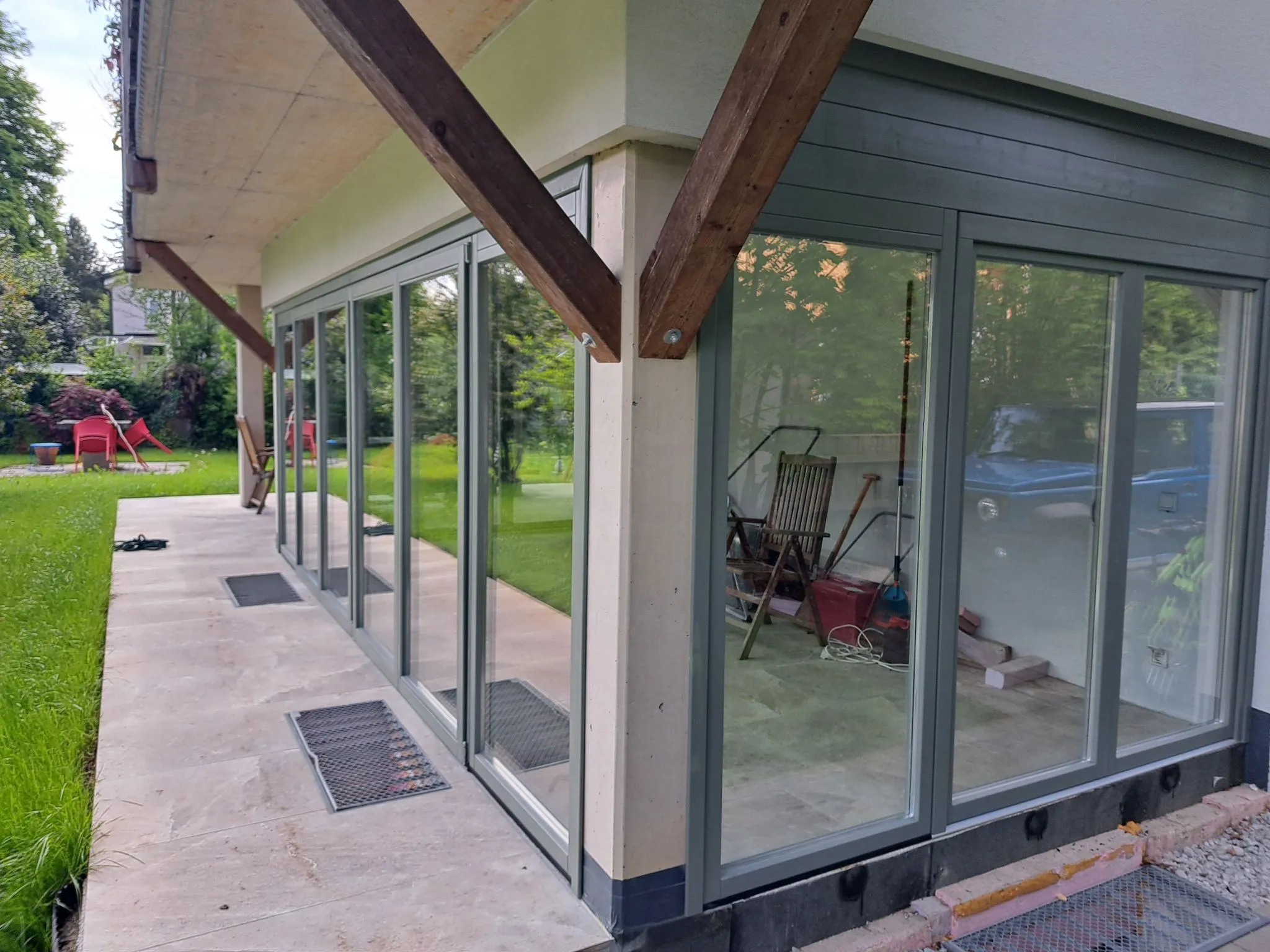 Haus mit großen bodentiefen Fenstern und einer Terrasse mit Blick auf einen Garten mit Gartenmöbeln.