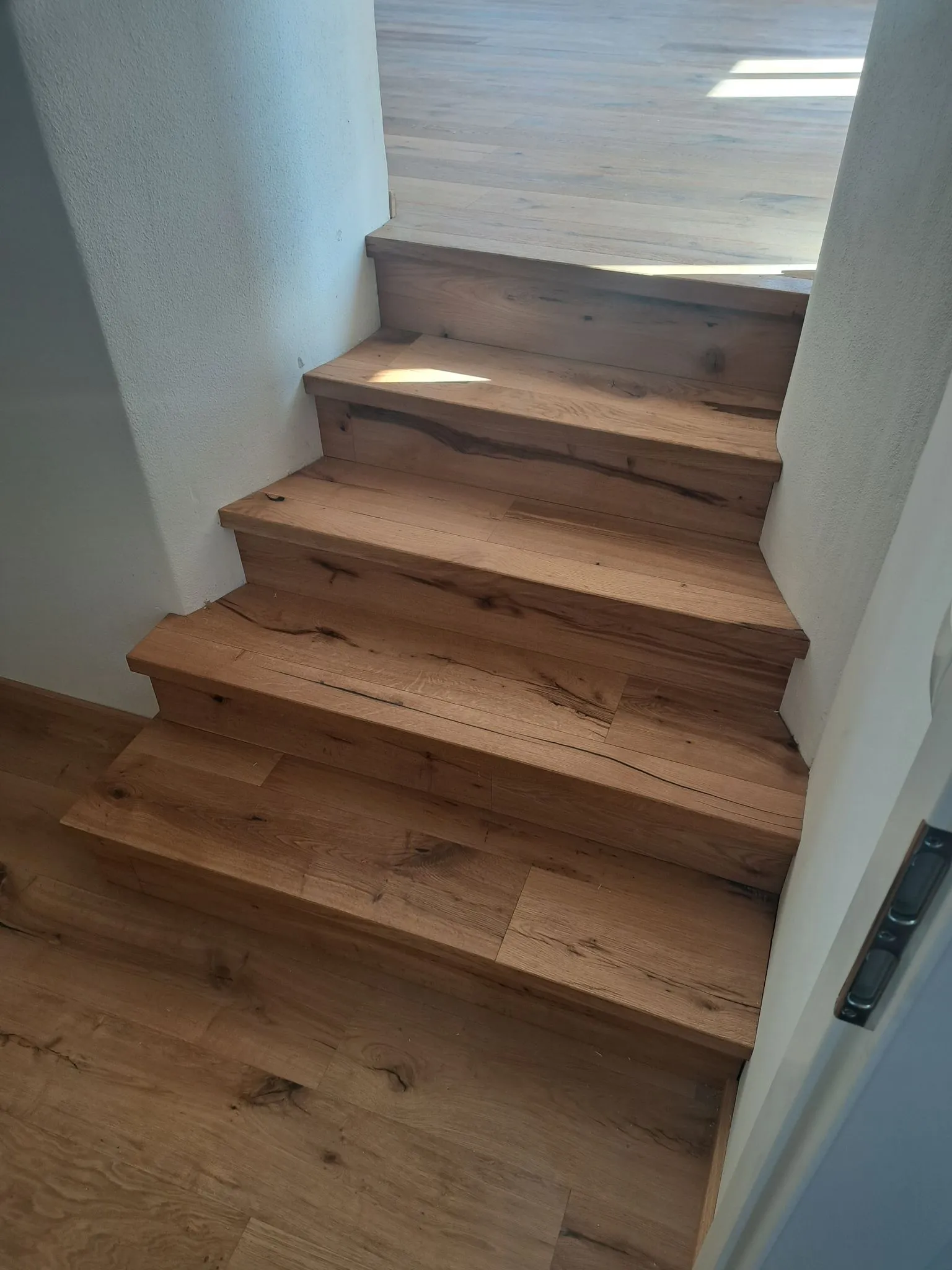 Holztreppe mit vier Stufen zwischen weißen Wänden und Holzboden.