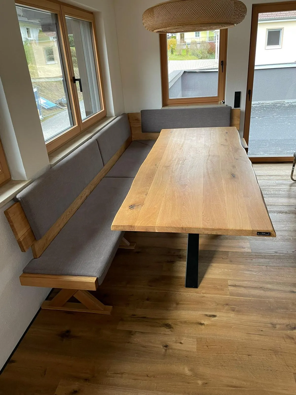 Essbereich mit einer Eckbank aus Holz und grauer Polsterung sowie einem großen Holztisch mit schwarzem Metallbein.