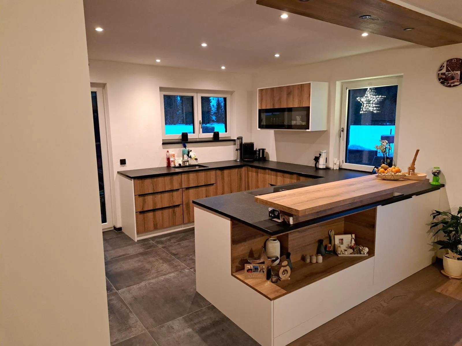 Moderne U-förmige Küche mit Holzschränken, schwarzer Arbeitsplatte und dekorativen Elementen in einem hell beleuchteten Raum.