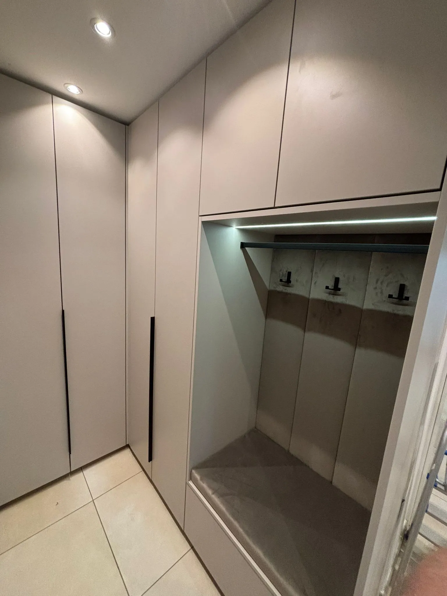 Moderner begehbarer Kleiderschrank mit grauen Schranktüren, eingebauter Sitzbank und LED-Beleuchtung.