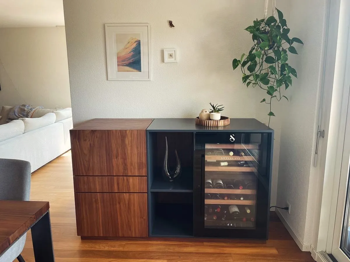 Moderner Wohnzimmerschrank mit Weinkühler, Holzschubladen, Deko-Vase, Pflanze auf einer Holzablage und hängender grüner Pflanze an der Wand.
