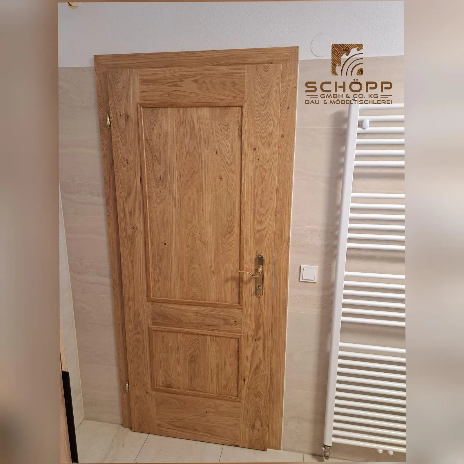 Massivholztür aus Eiche mit Messinggriff in einem Badezimmer neben einem weißen Handtuchheizkörper.