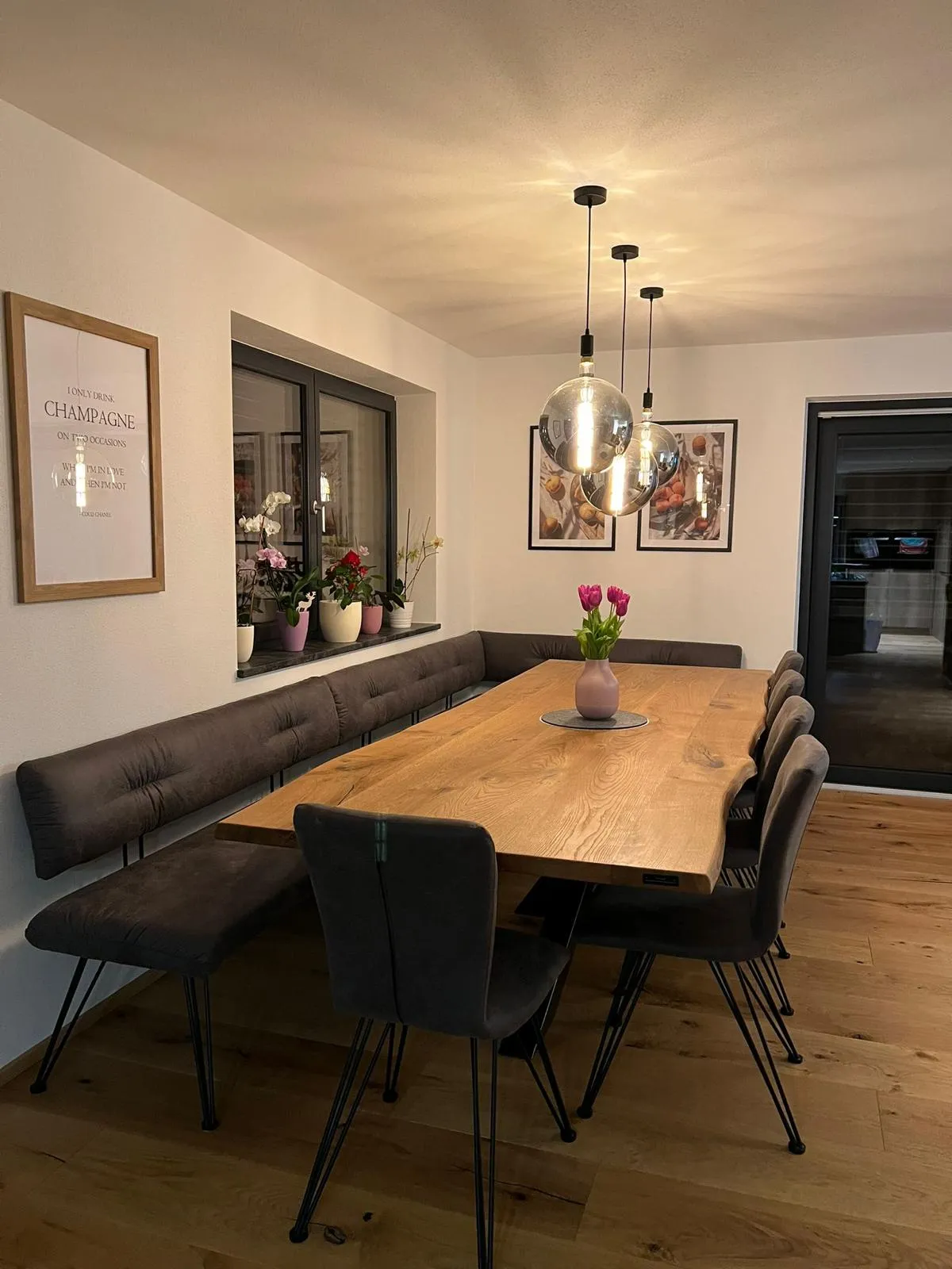 Moderner Essbereich mit einem großen Holztisch, schwarzen Stühlen, Bank, rosa Tulpen in Vase und modernen Hängeleuchten.