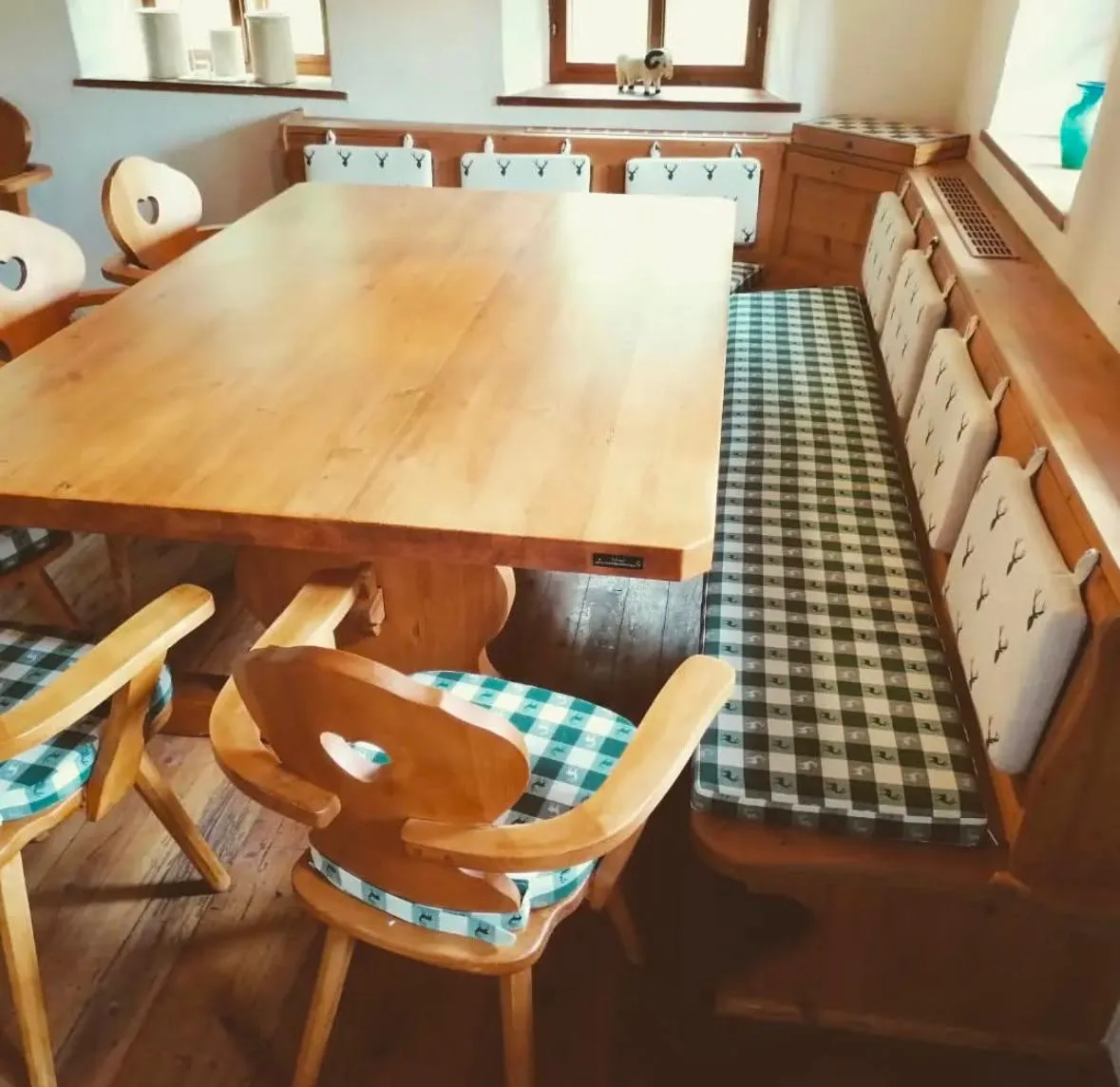 Rustikaler Essbereich mit einem großen Holztisch, Holzhockern mit Herzformen am Rücken und karierten Sitzpolstern neben einer gepolsterten Bank.