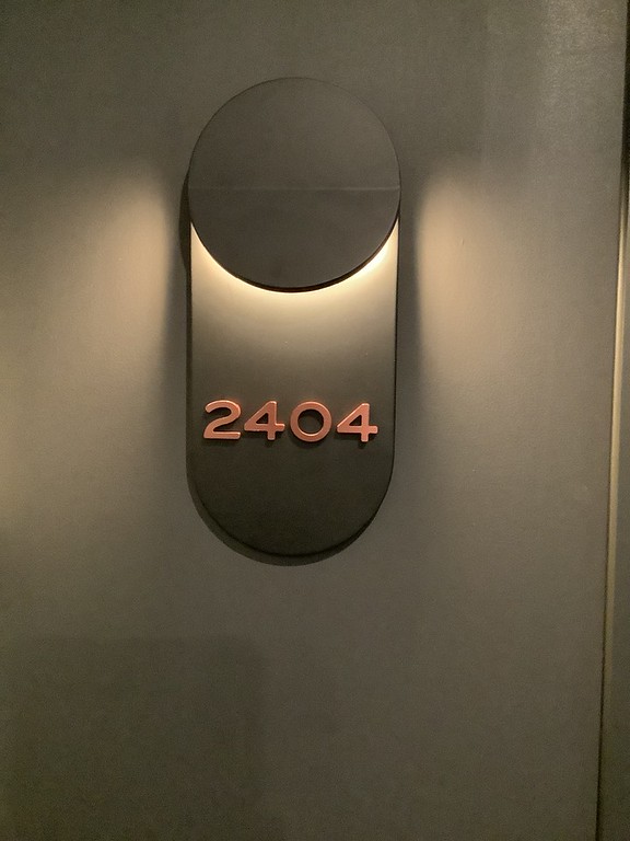 Copper dimensional room number 2404 on an uplit oval wall sconce