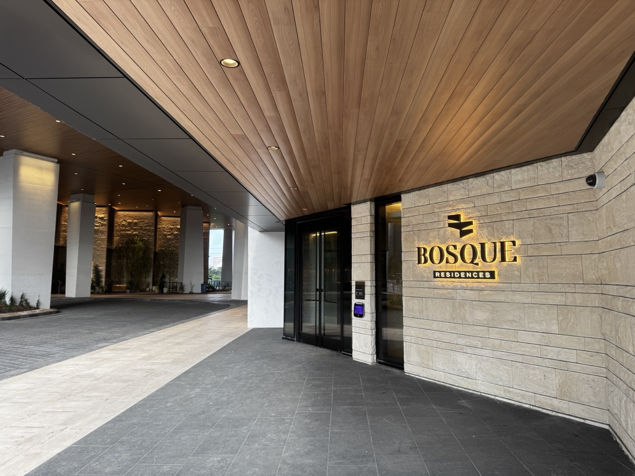 Illuminated dimensional Bosque Residences logo on a stone wall beneath the entrance canopy