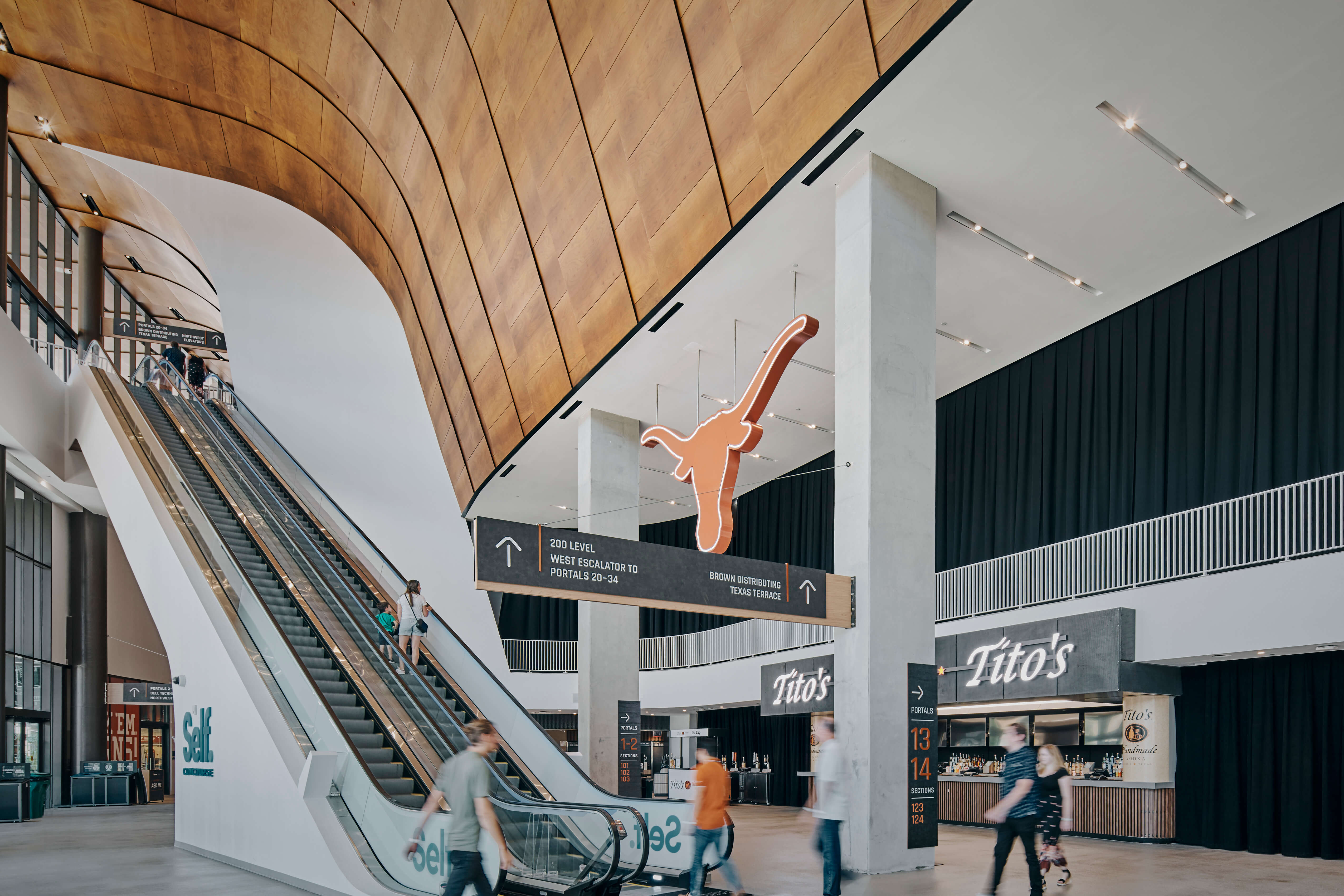 Suspended Longhorn logo sign and directional wayfinding above the Moody Center concourse