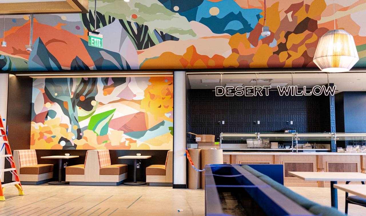Illustrated desert mural above booth seating beside an illuminated Desert Willow dining sign