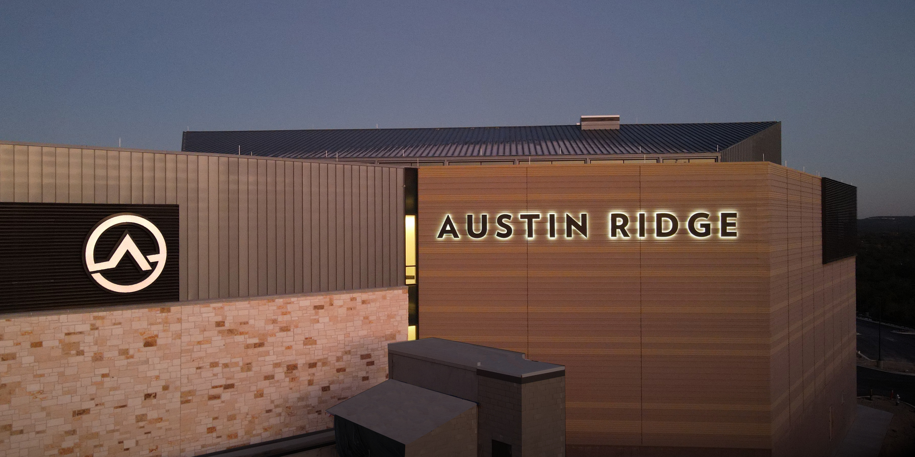 Illuminated Austin Ridge channel letters and circular logo on the exterior facade at dusk