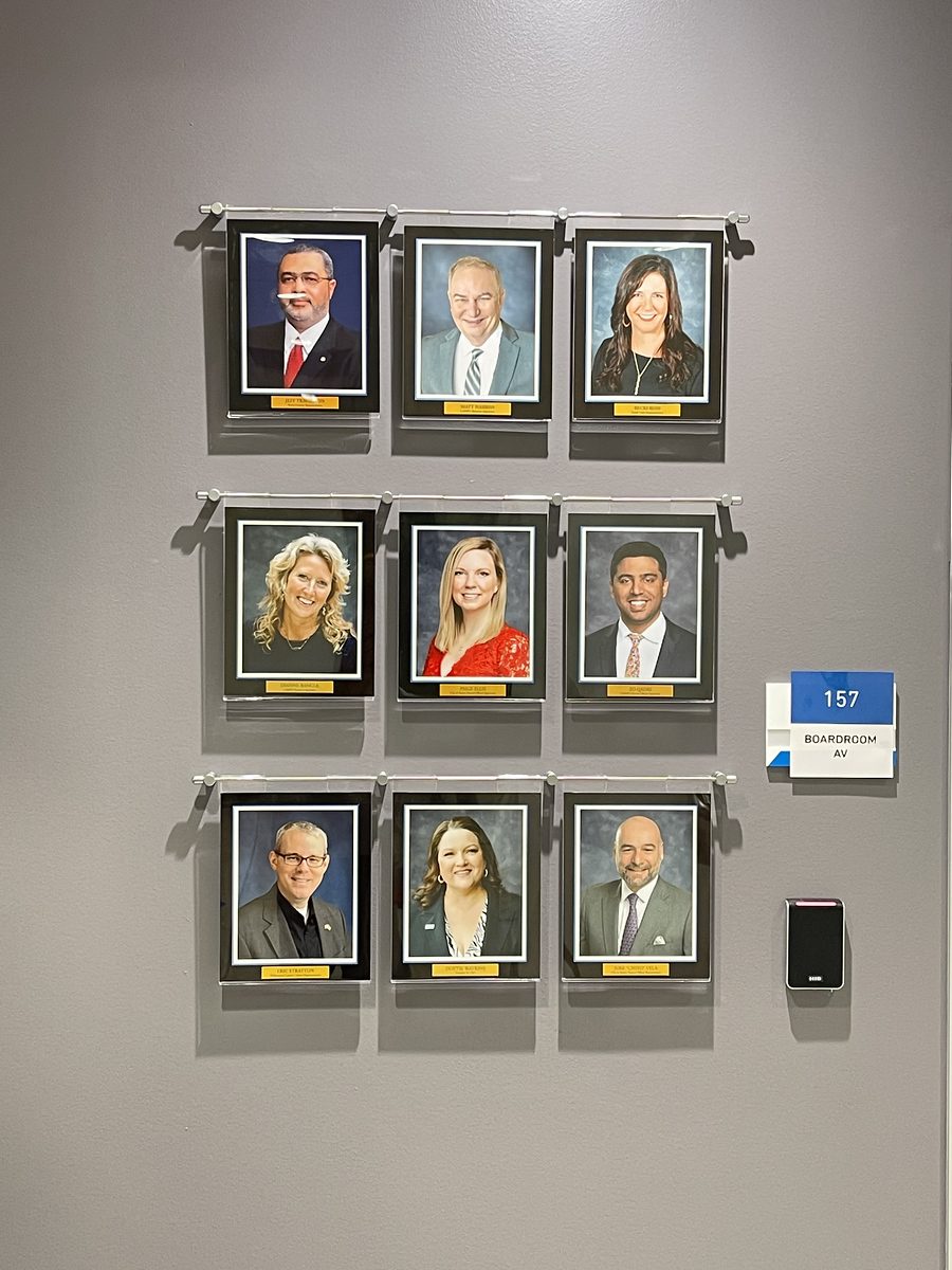 Framed board member portrait wall beside a room identification sign