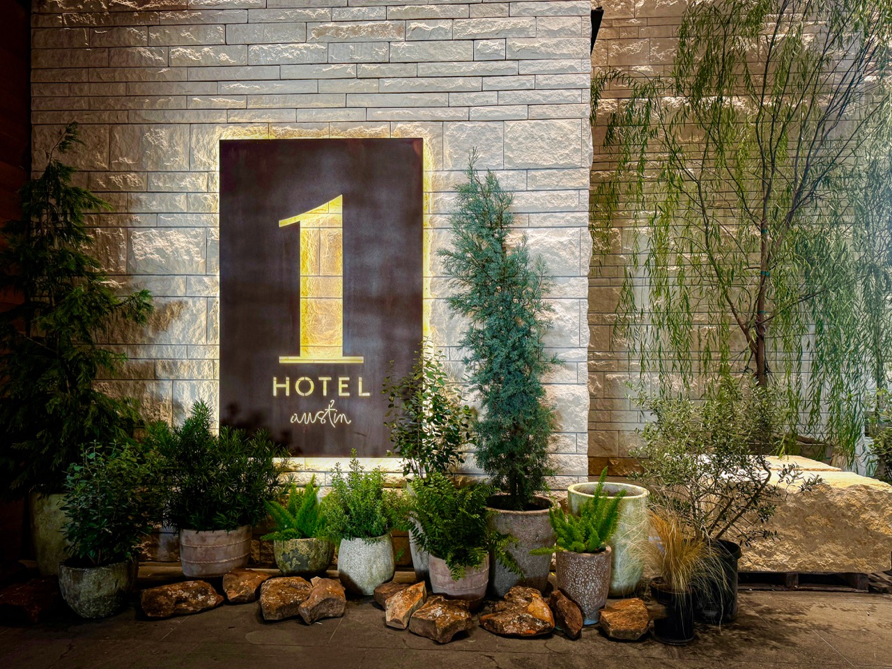 Backlit 1 Hotel Austin metal panel sign surrounded by potted plants at night