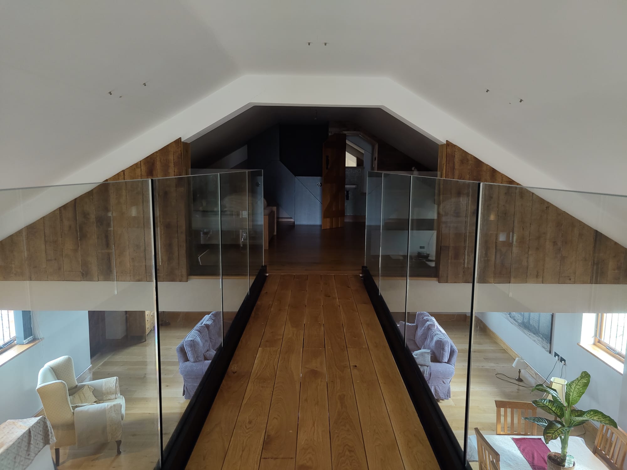 A wooden walkway with glass railings inside a loft space, leading to a living area.