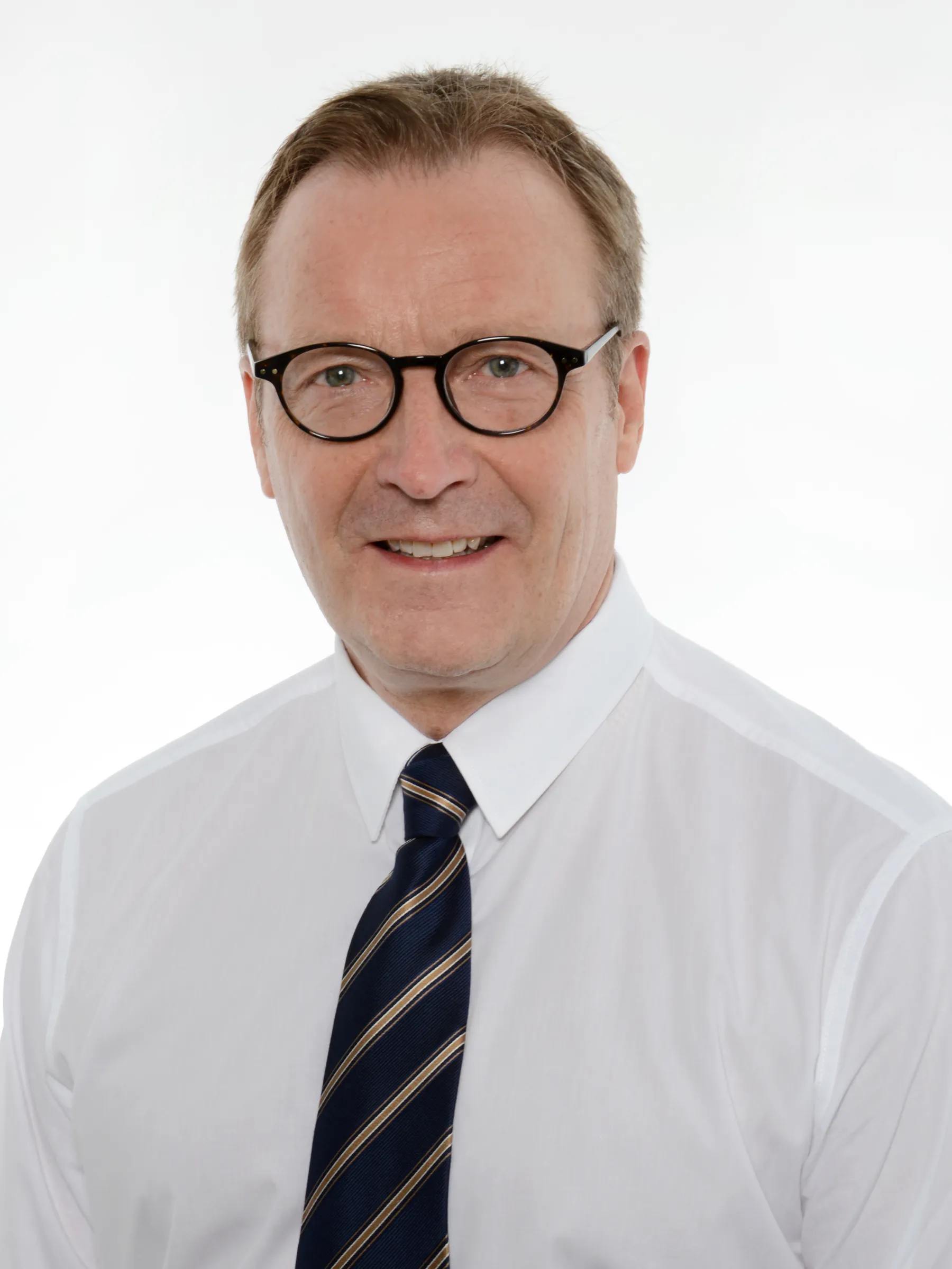 Muotokuva miehestä, jolla on silmälasit, valkoinen paita ja sininen solmio, valkoisella taustalla, tasaisessa valaistuksessa.