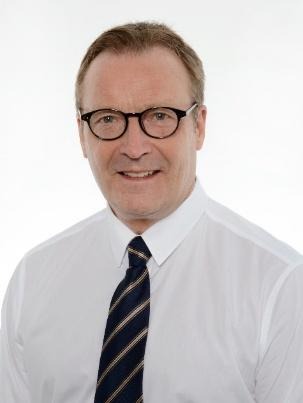 Keskellä oleva mies, jolla on silmälasit, valkoinen paita ja raidallinen solmio, valkoisella taustalla.