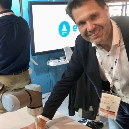Man met badge buigt zich voorover en raakt een robotarm aan bij een evenementstand.