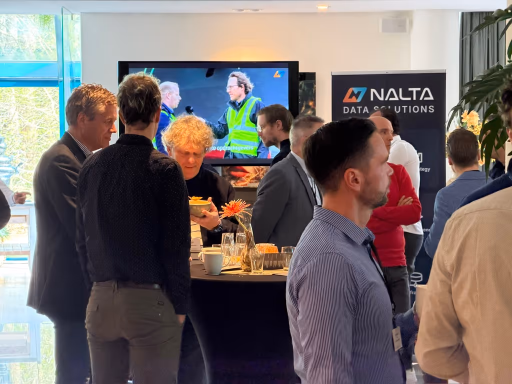 Groep mannen praten in een lichte ruimte met een NALTA-data-oplossingen banner achter hen.