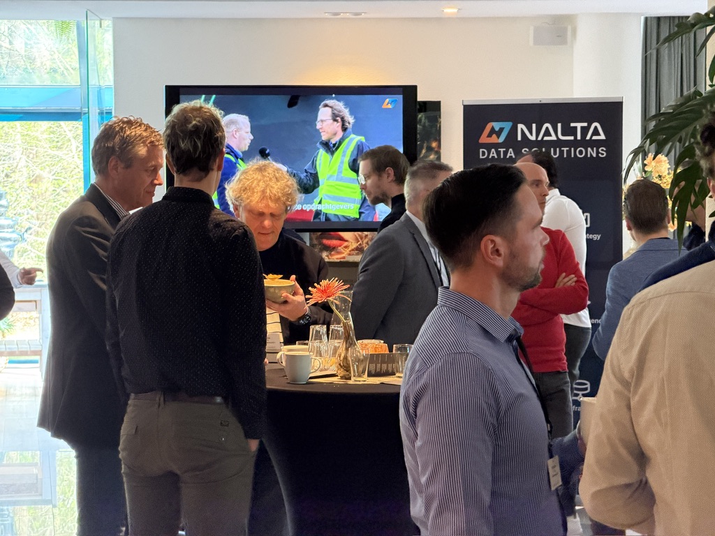Groep mannen praten in een lichte ruimte met een NALTA-data-oplossingen banner achter hen.