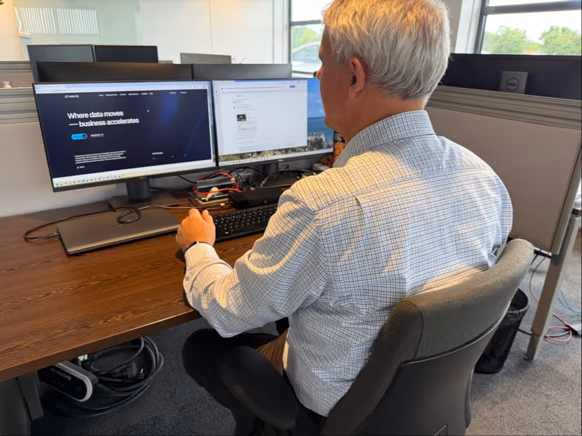 Man zit achter bureau en werkt op computer met twee monitoren in een modern kantoor.