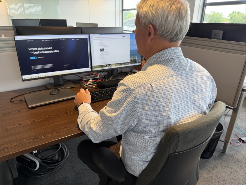 Man zit achter bureau en werkt op computer met twee monitoren in een modern kantoor.