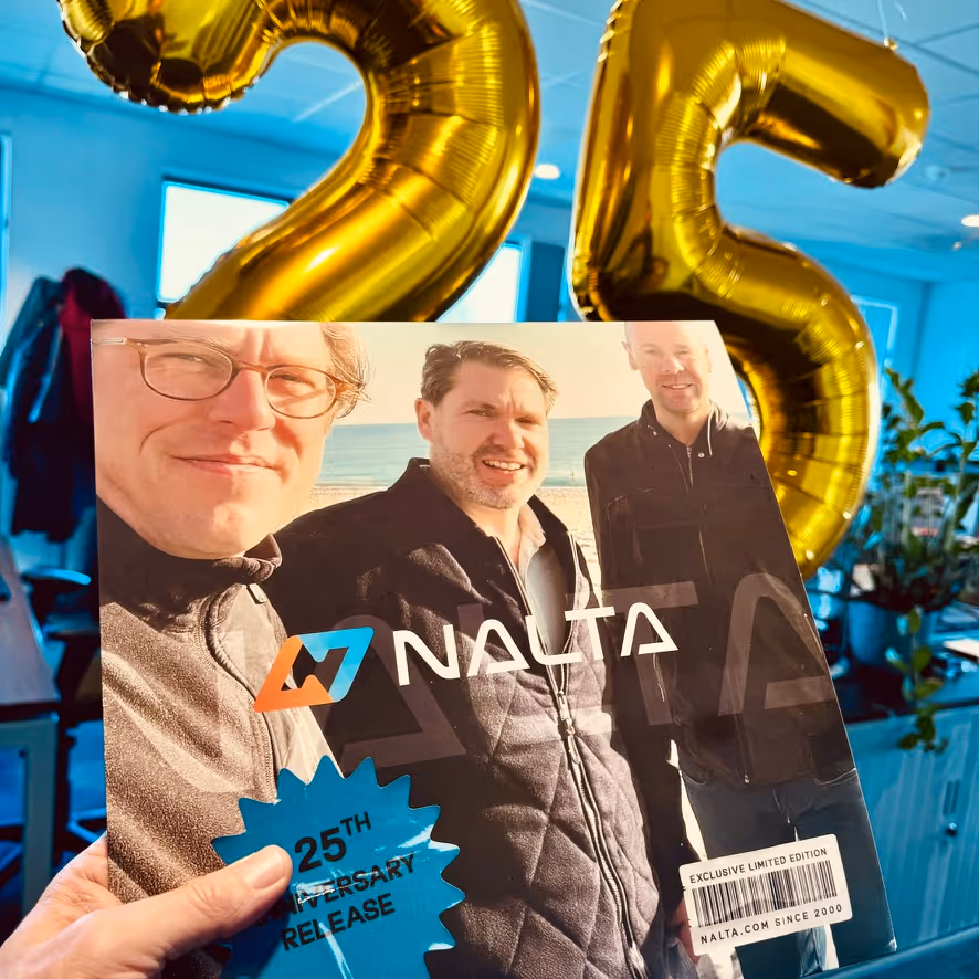 Hand houdt Nalata 25-jarig jubileumeditie met portret van drie mannen en gouden ballonnen '25'.