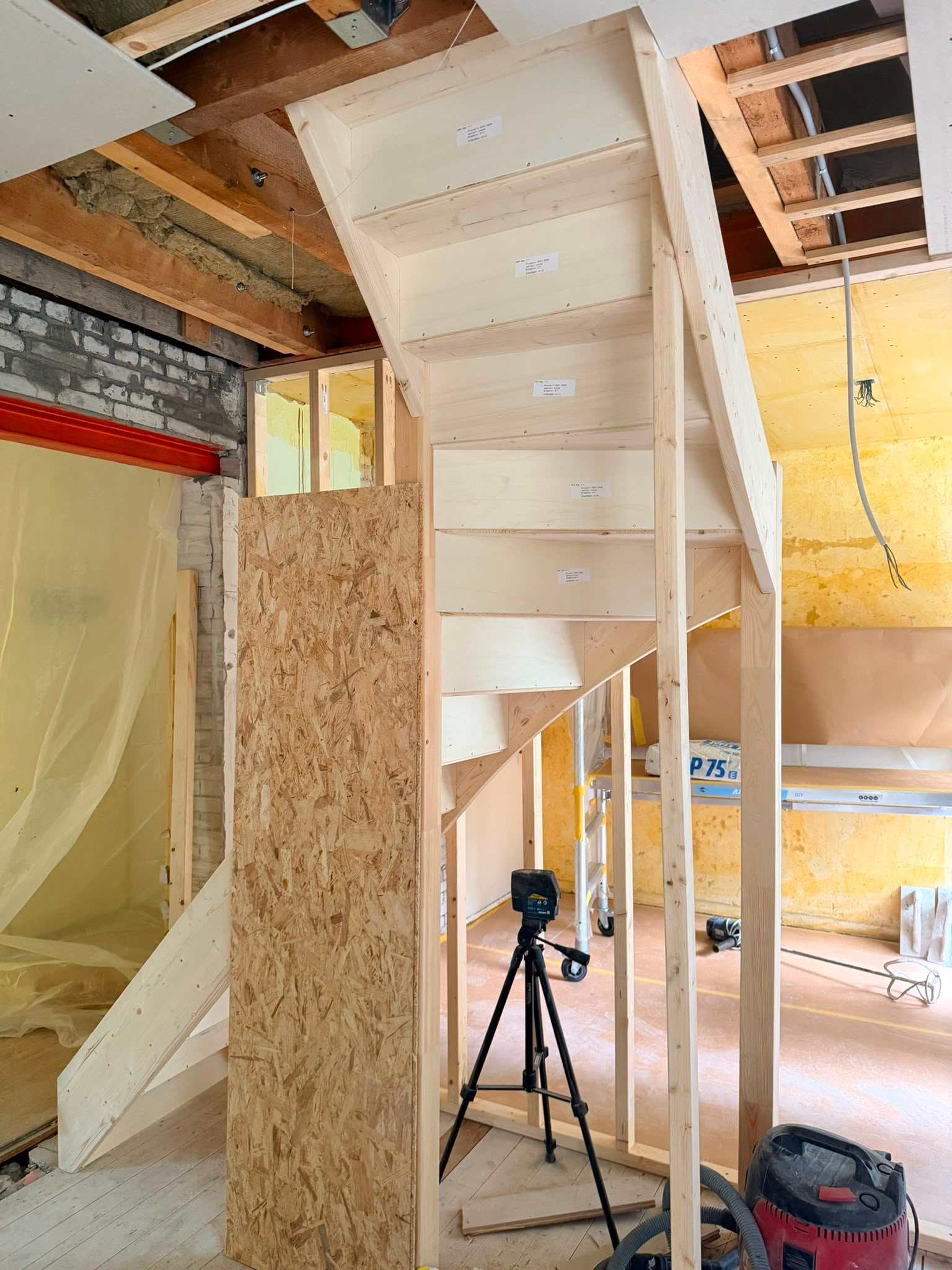 Wooden ceiling beams with metal brackets installed for roof reinforcement, with a hanging light bulb and exposed wiring.