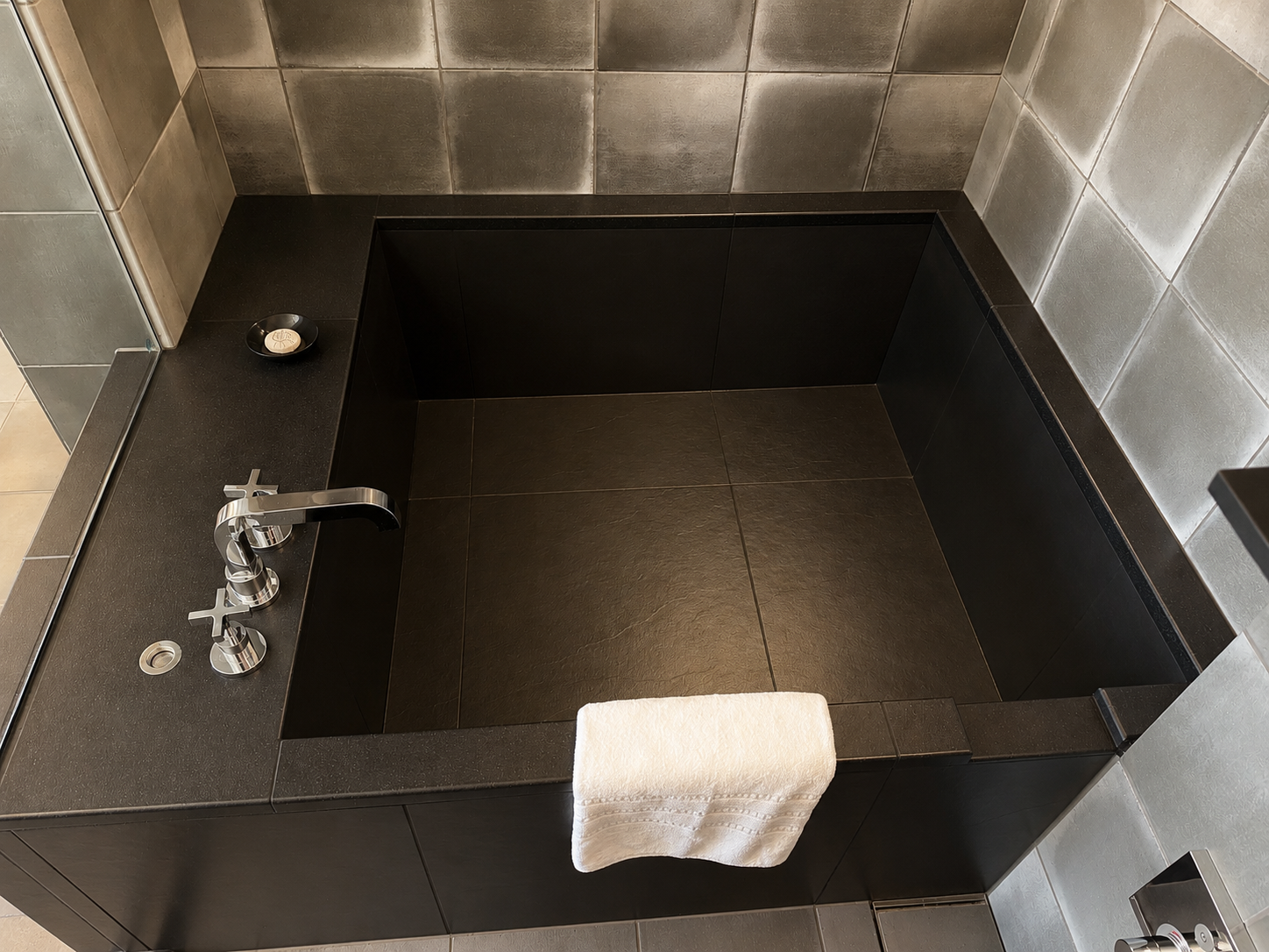 Deep Japanese soaking tub in a Gensui guest room at Four Seasons Osaka, finished with dark stone and silver wall tiles.