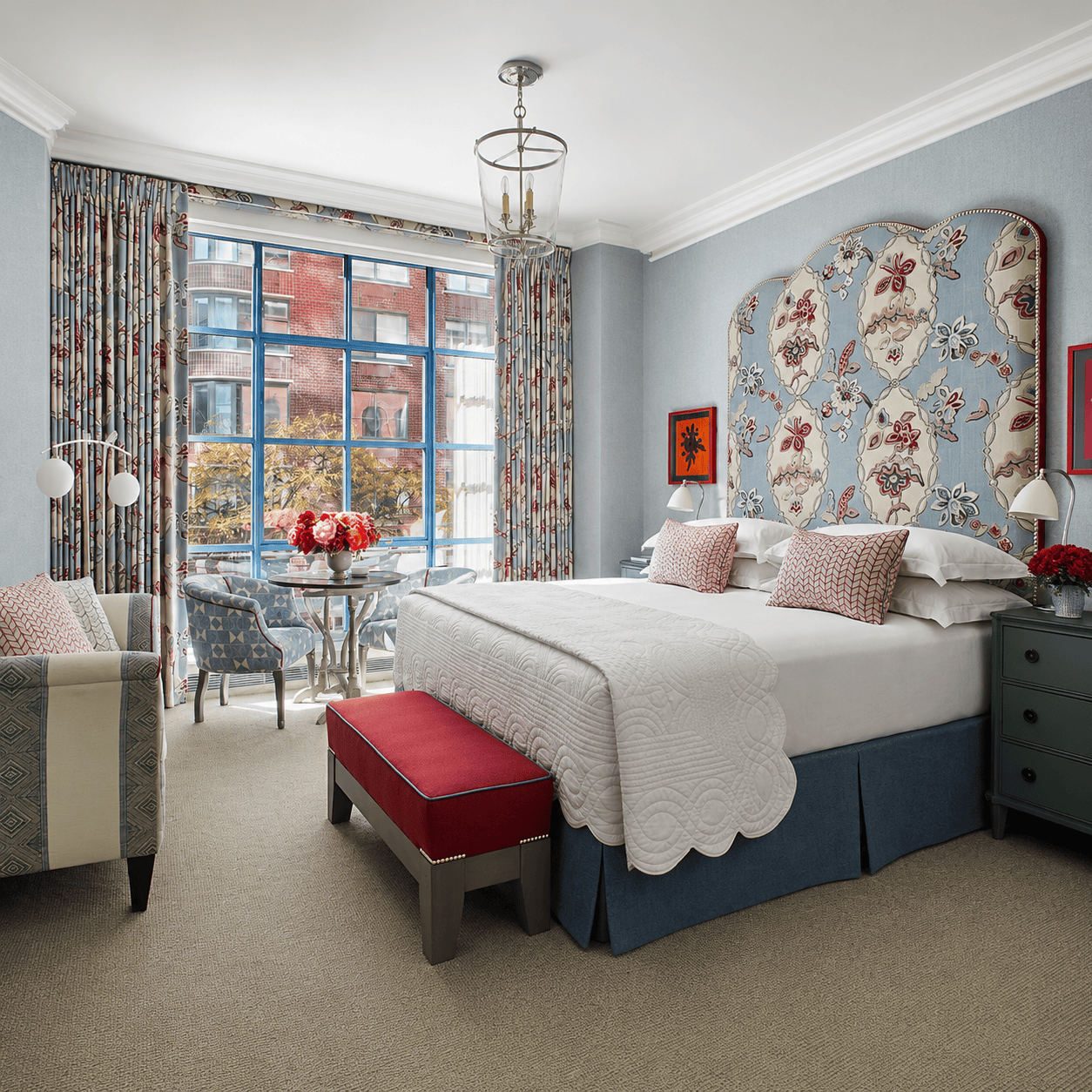 Colorful Firmdale hotel bedroom with patterned headboard, large window and seating area in London.