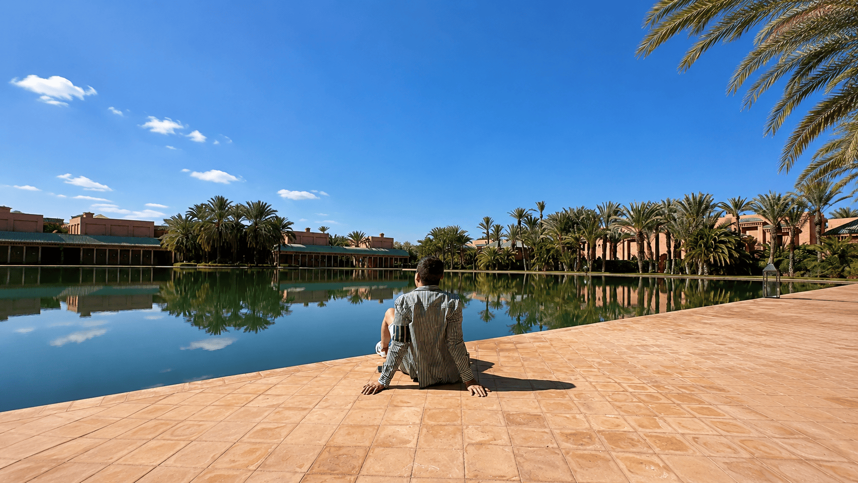 Dylan Clements beside the reflecting pools at Amanjena in Marrakech, Morocco surrounded by palm trees and Moorish architecture.