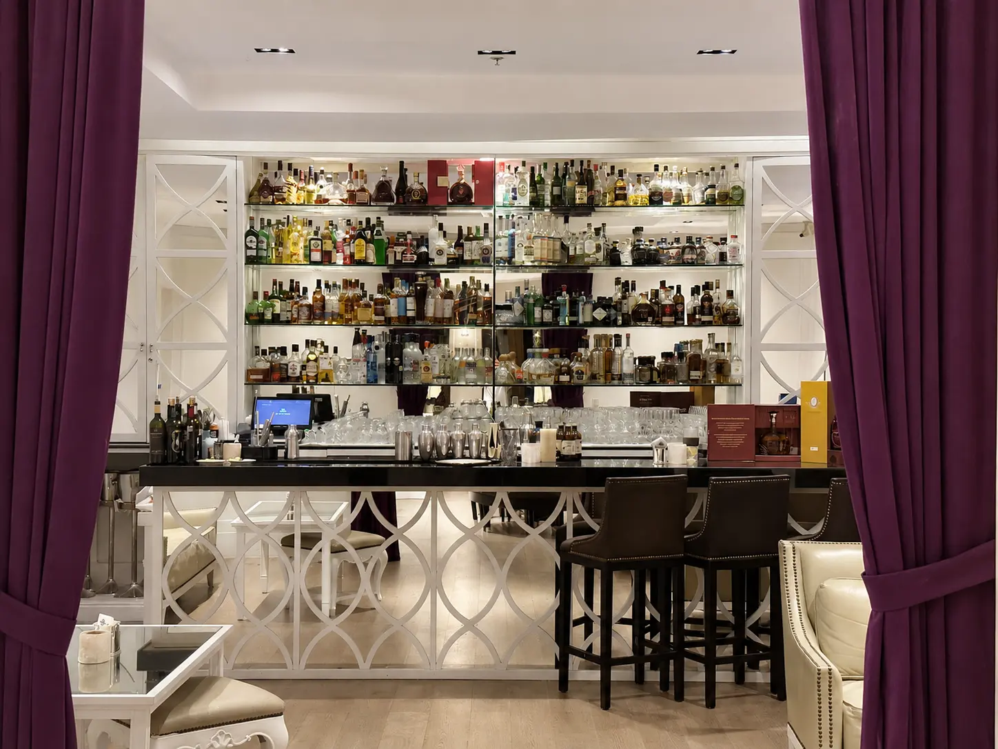 The bar inside Carolina restaurant at The St. Regis Punta Mita, framed by purple curtains and lined with bottles of spirits.