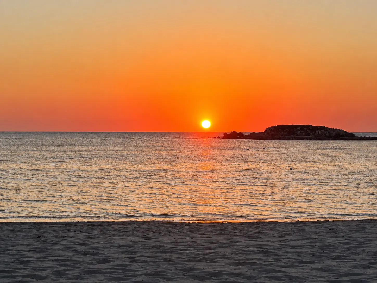 Sunset over the Pacific Ocean at The St. Regis Punta Mita with the sun setting beside rocky outcrops and reflecting across calm water.