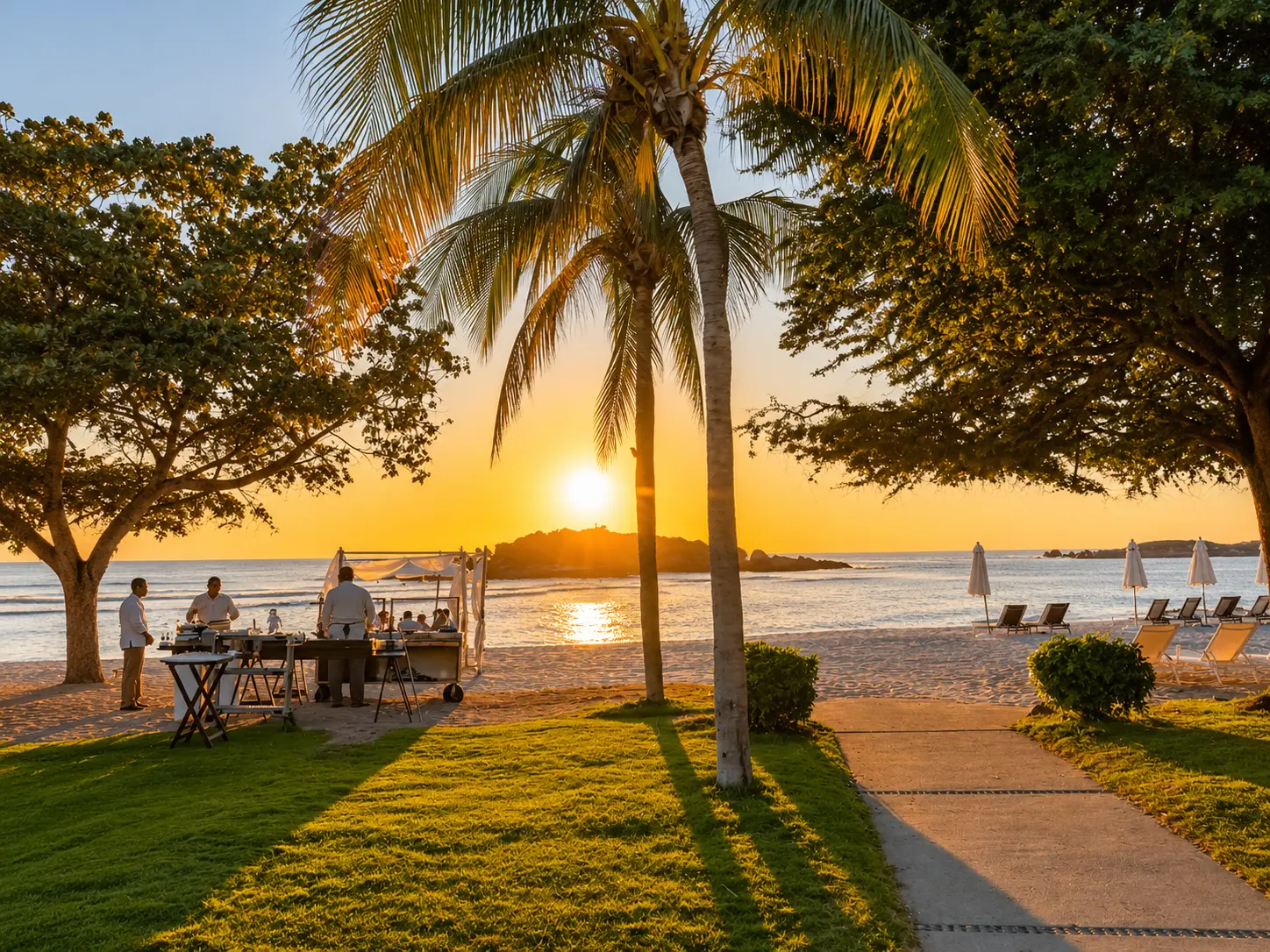 Sunset over the Pacific Ocean at The St. Regis Punta Mita with palm trees, beach loungers, and staff preparing an evening dining setup.