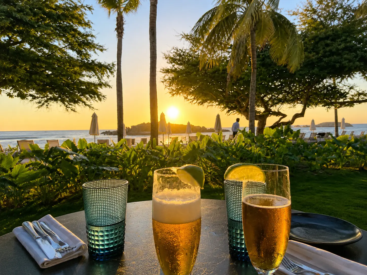 Two drinks with lime served at sunset at The St. Regis Punta Mita, overlooking palm trees, the beach, and the Pacific Ocean.