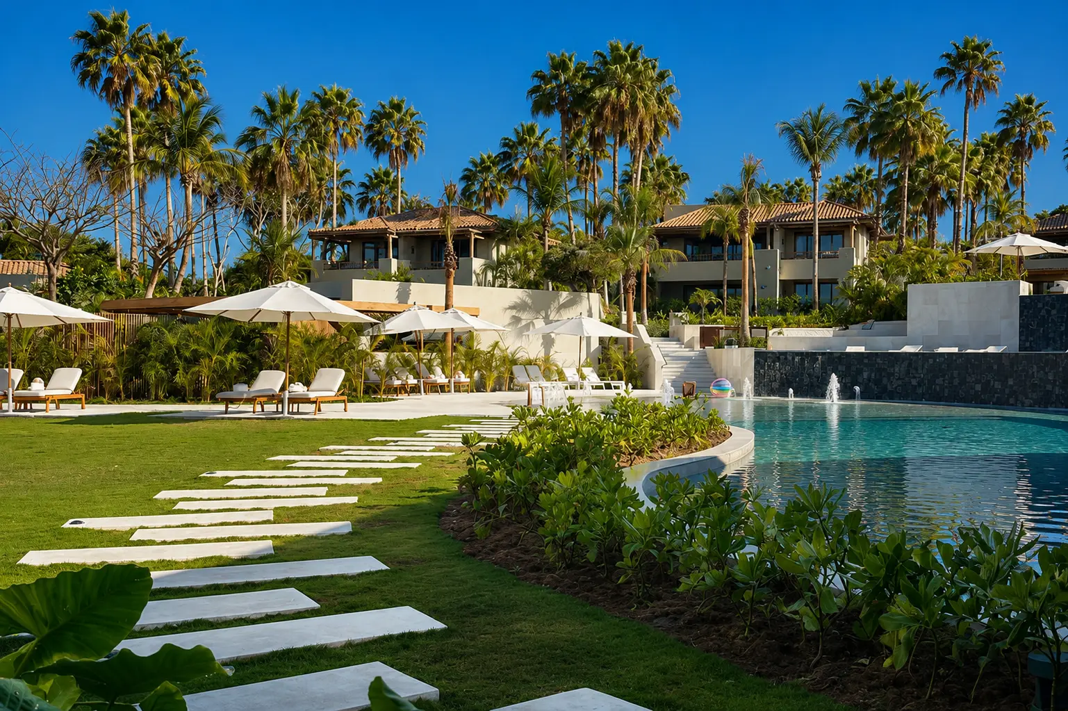 Family swimming pool at The St. Regis Punta Mita surrounded by palm trees, sun loungers, landscaped gardens, and resort buildings.