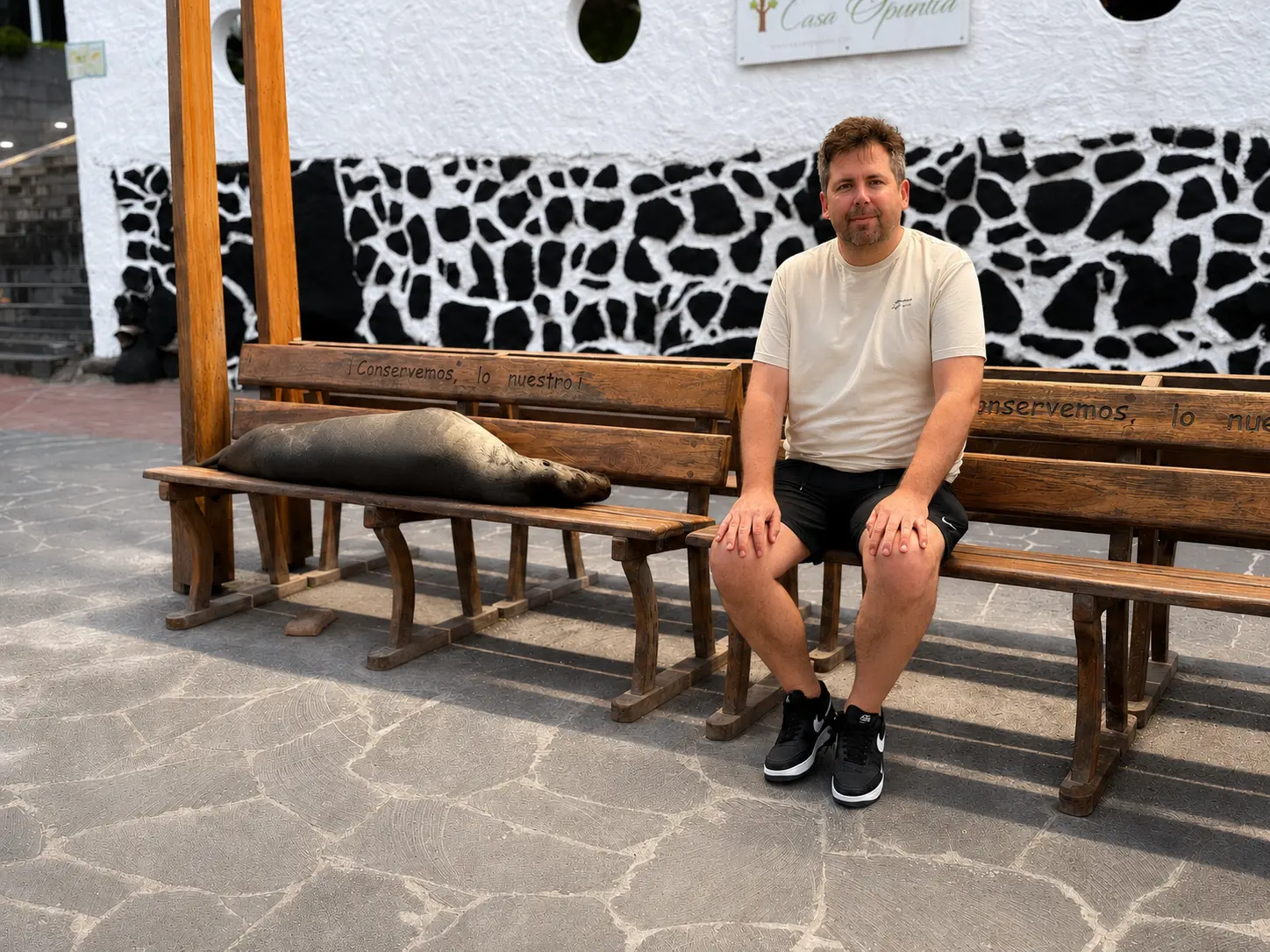 Dylan Clements, founder of Clements Travel, sitting beside a sleeping Galápagos sea lion on a bench in San Cristóbal, Galápagos Islands.
