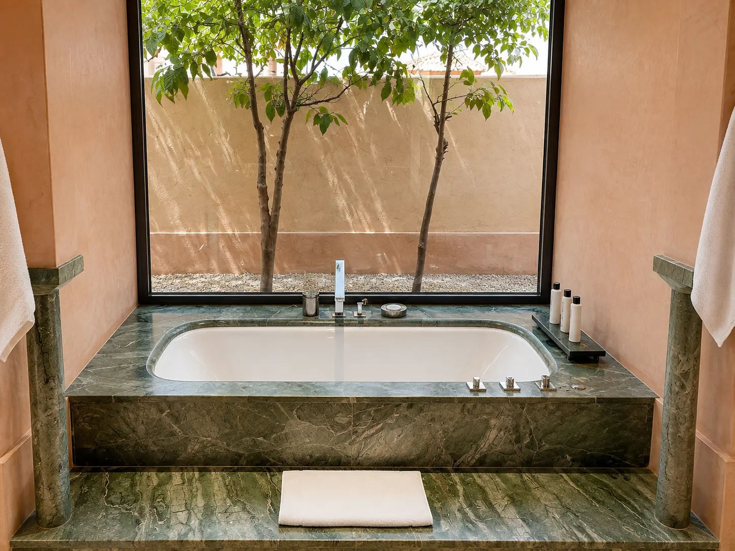Deep soaking tub in the bathroom of a Deluxe Pavilion at Amanjena Marrakech, framed by green marble and a private courtyard view.