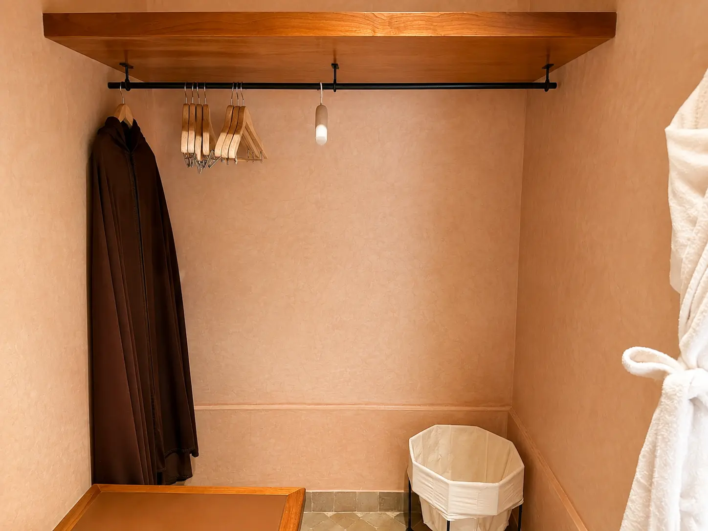 Walk-in dressing area inside a Deluxe Pavilion at Amanjena Marrakech with wooden hangers, robes, luggage bench, and laundry basket.