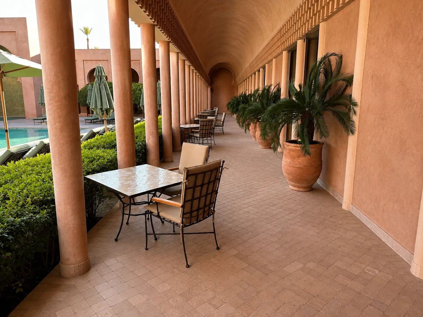 The outdoor terrace at Arva restaurant at Amanjena in Marrakech, with terracotta columns, vaulted walkways, poolside tables, and traditional Moroccan architecture.