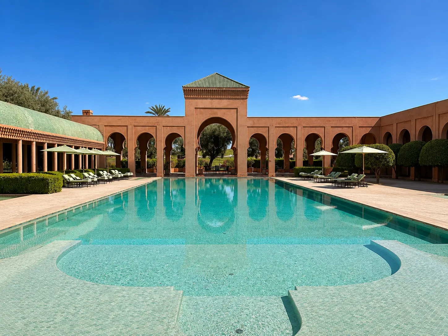 Main swimming pool at Amanjena in Marrakech with Moroccan arches, palm-lined courtyards, shaded loungers, and turquoise water.