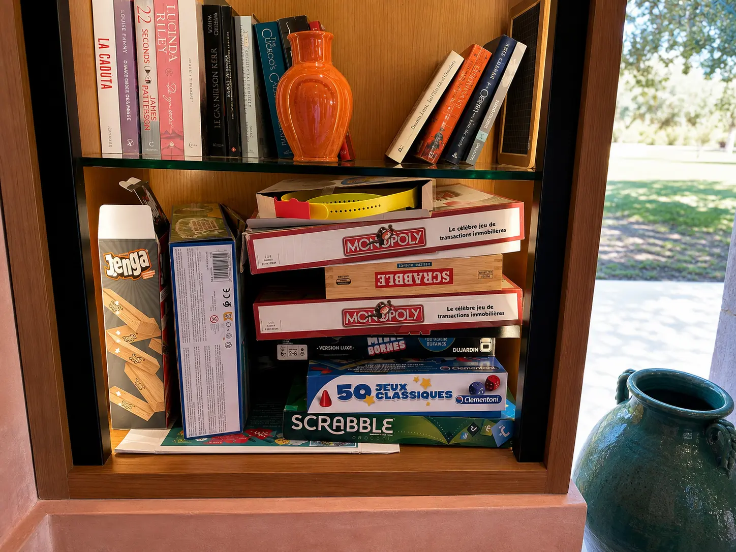 A bookshelf at Amanjena in Marrakech stocked with books and classic board games including Monopoly, Scrabble, and Jenga for guests to enjoy.
