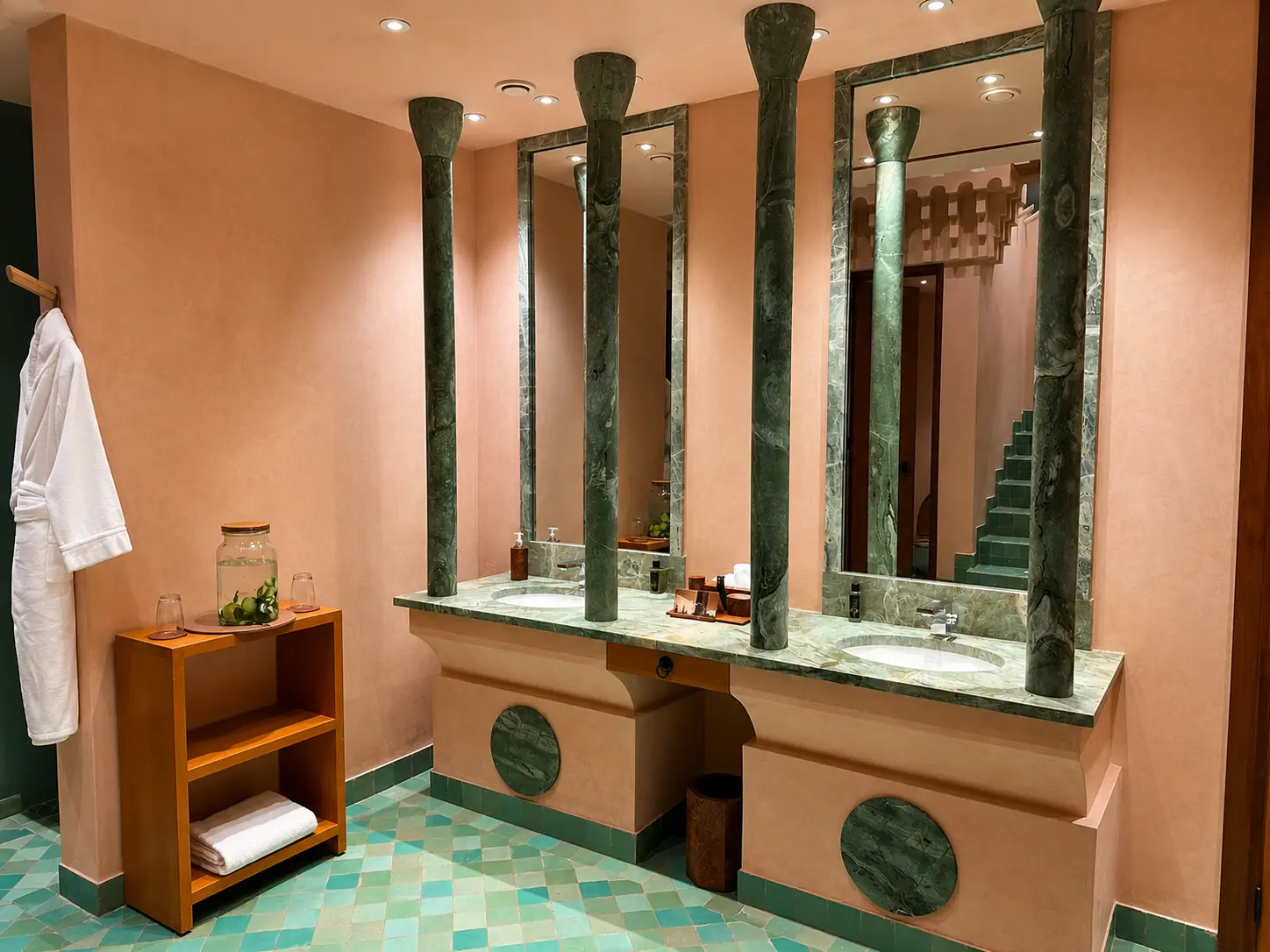 Bathroom inside Amanjena’s spa in Marrakech with green marble columns, twin sinks, rose-colored walls, and turquoise Moroccan floor tiles.