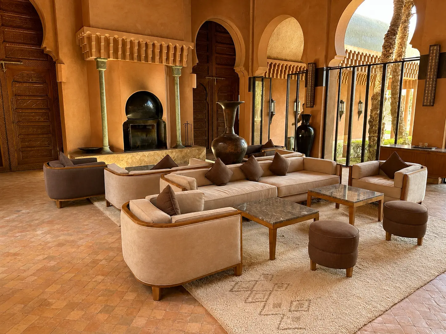 The elegant lobby lounge at Amanjena in Marrakech featuring Moroccan arches, a grand fireplace, handcrafted wooden doors, contemporary seating, and traditional North African design.