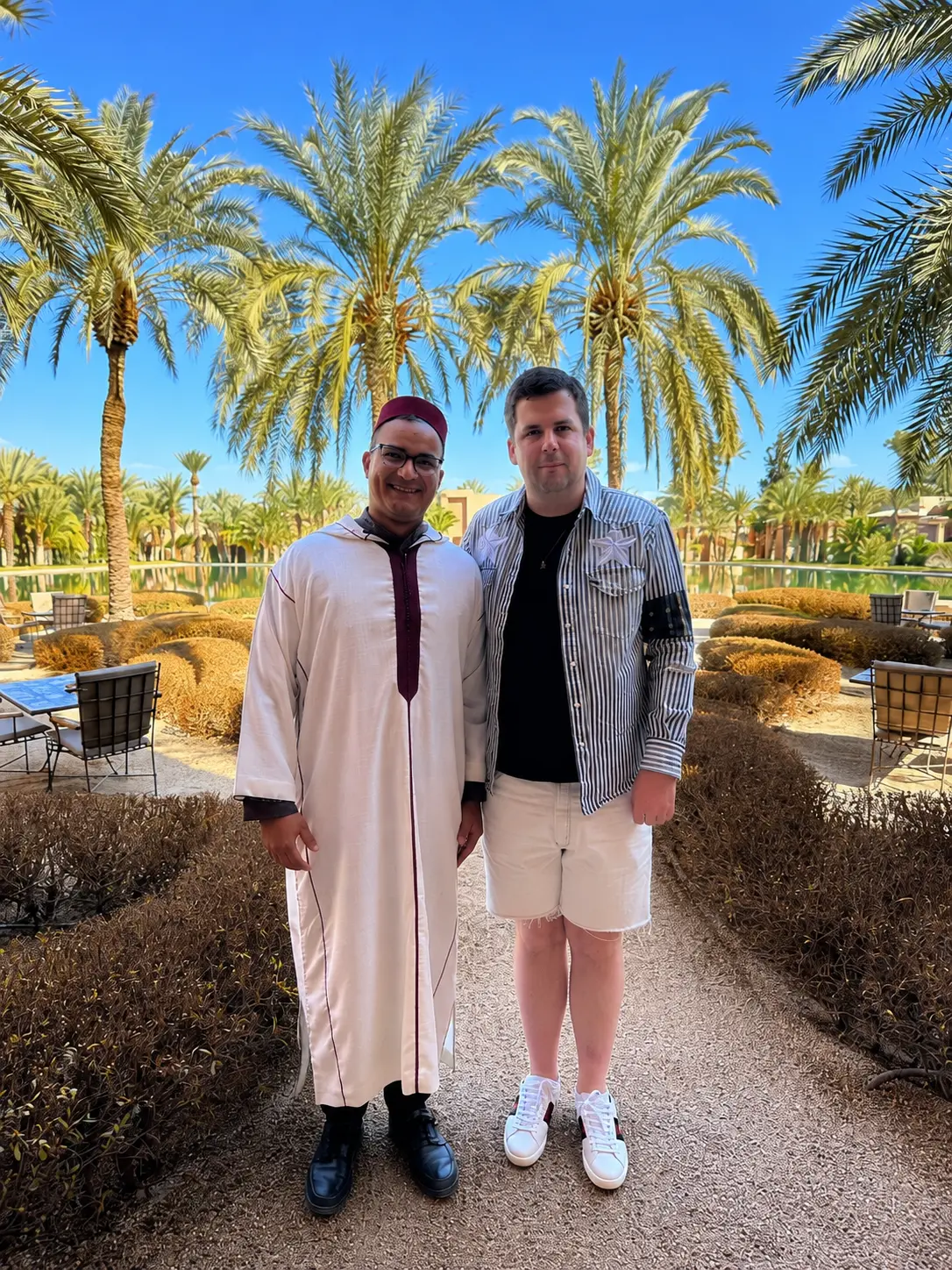 Guest with a member of the Amanjena team in the resort's palm-lined gardens beside the reflecting pool in Marrakech, Morocco.