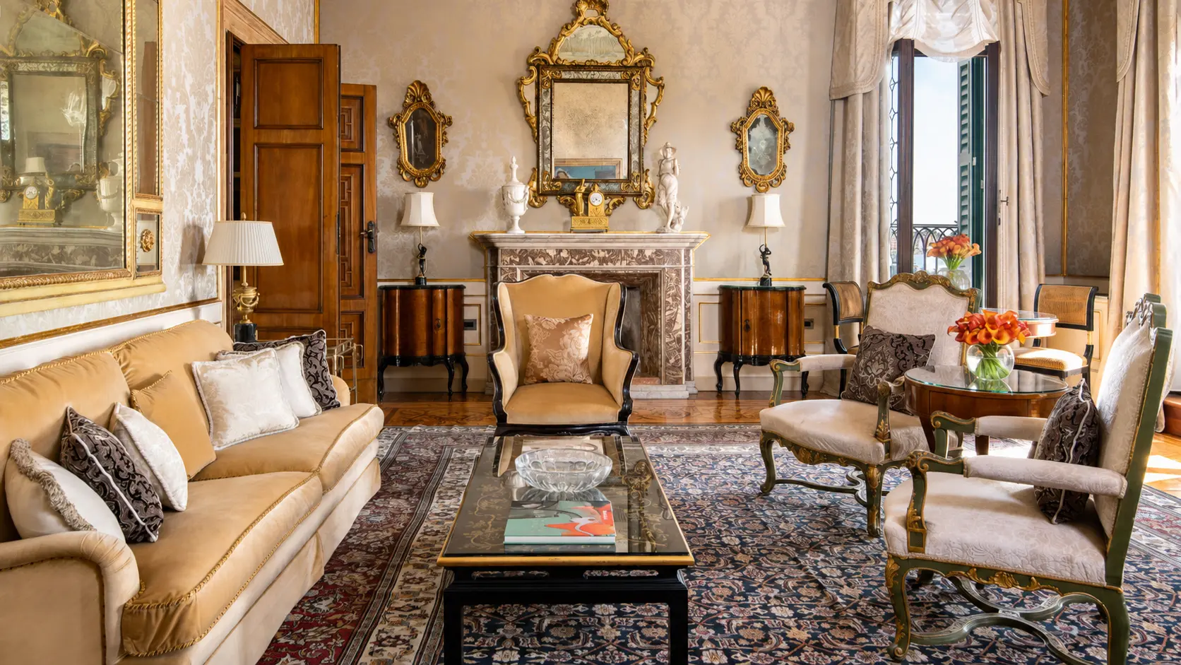 Ornate specialty suite living room at Four Seasons Hotel Danieli in Venice, with antique furnishings, gilded mirrors and a marble fireplace.