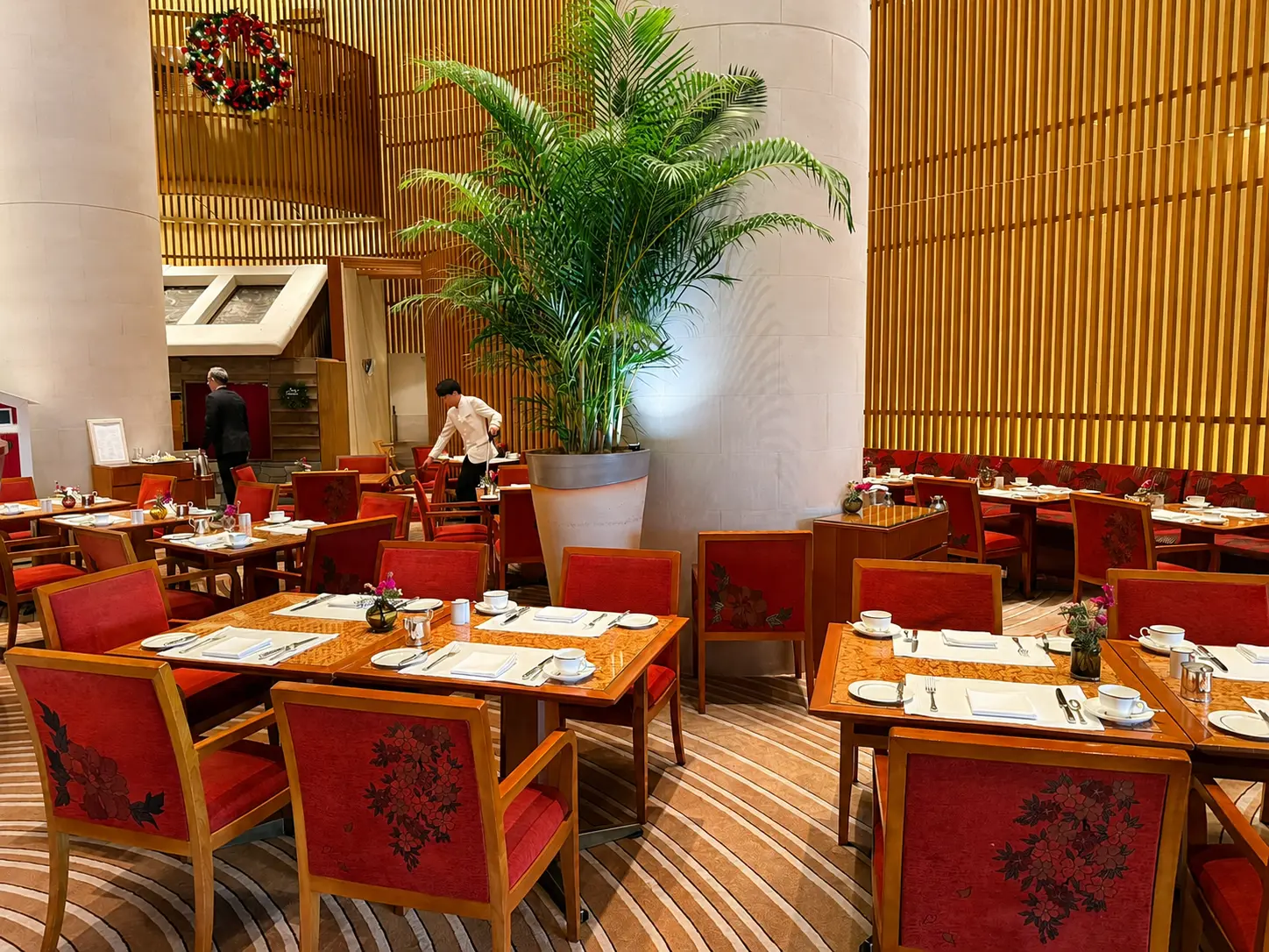 The Lobby restaurant at The Peninsula Tokyo with red seating, wood detailing and a large central palm.