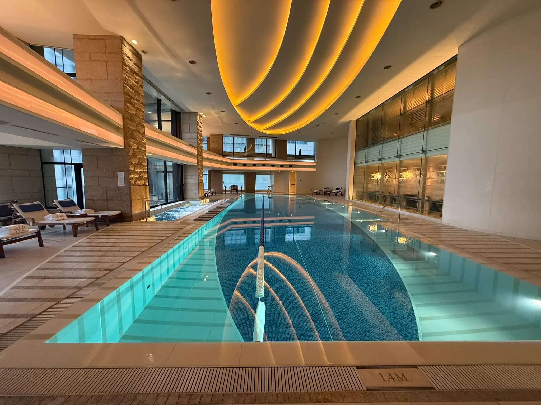 Indoor swimming pool at The Peninsula Tokyo spa with loungers, jacuzzi and illuminated ceiling.