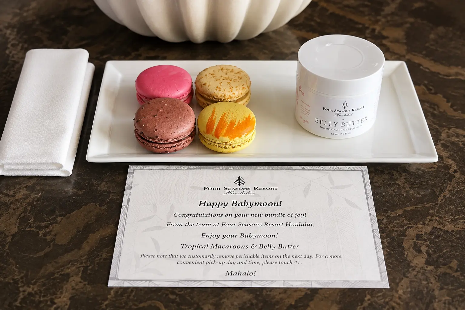 Four Seasons Hualalai babymoon amenity with tropical macarons and Hualalai Belly Butter arranged for Clements Travel clients.