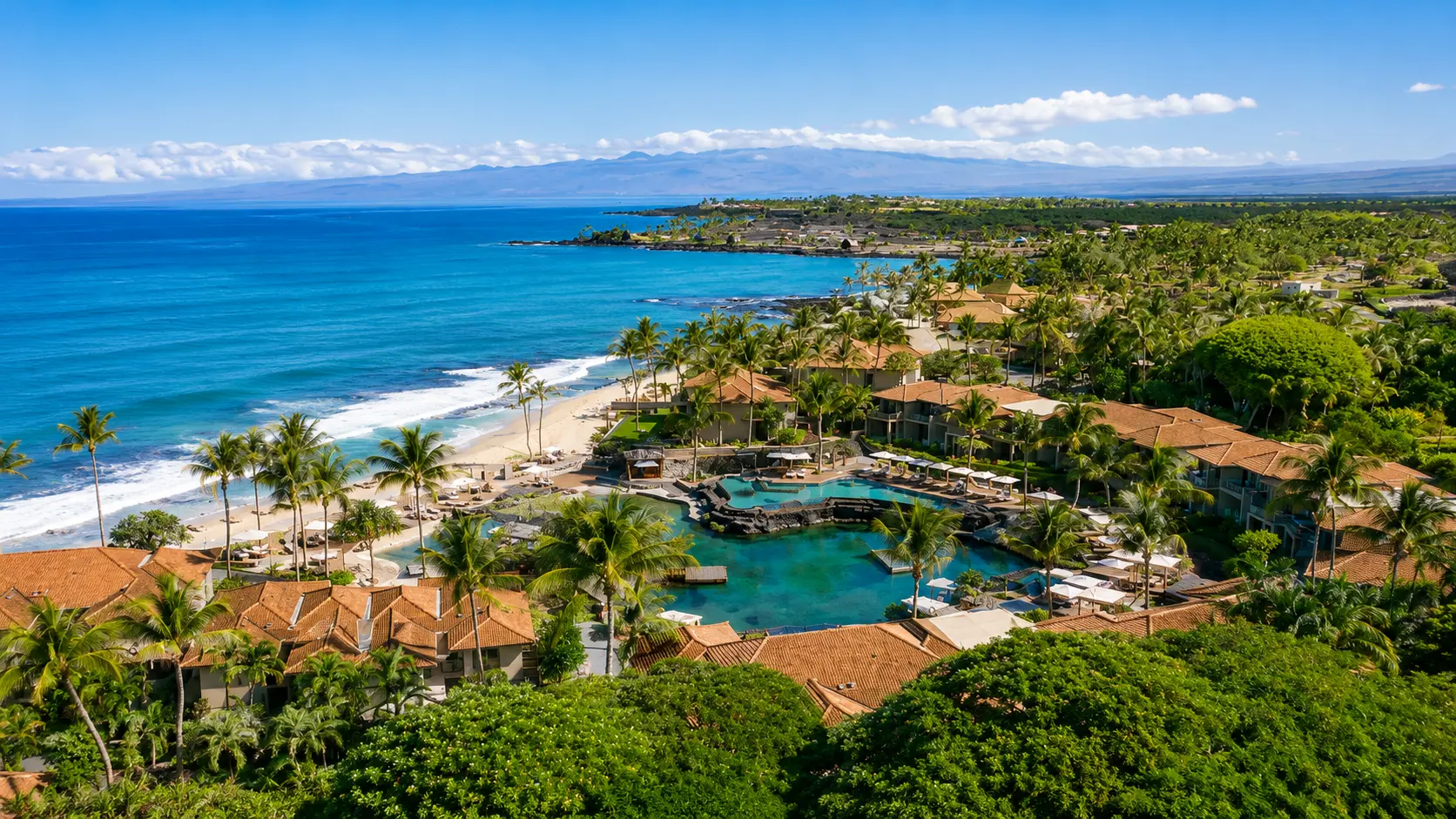 Aerial view of Four Seasons Resort Hualalai on Hawaii’s Big Island, showing the beachfront resort, lagoon, pools and tropical grounds.