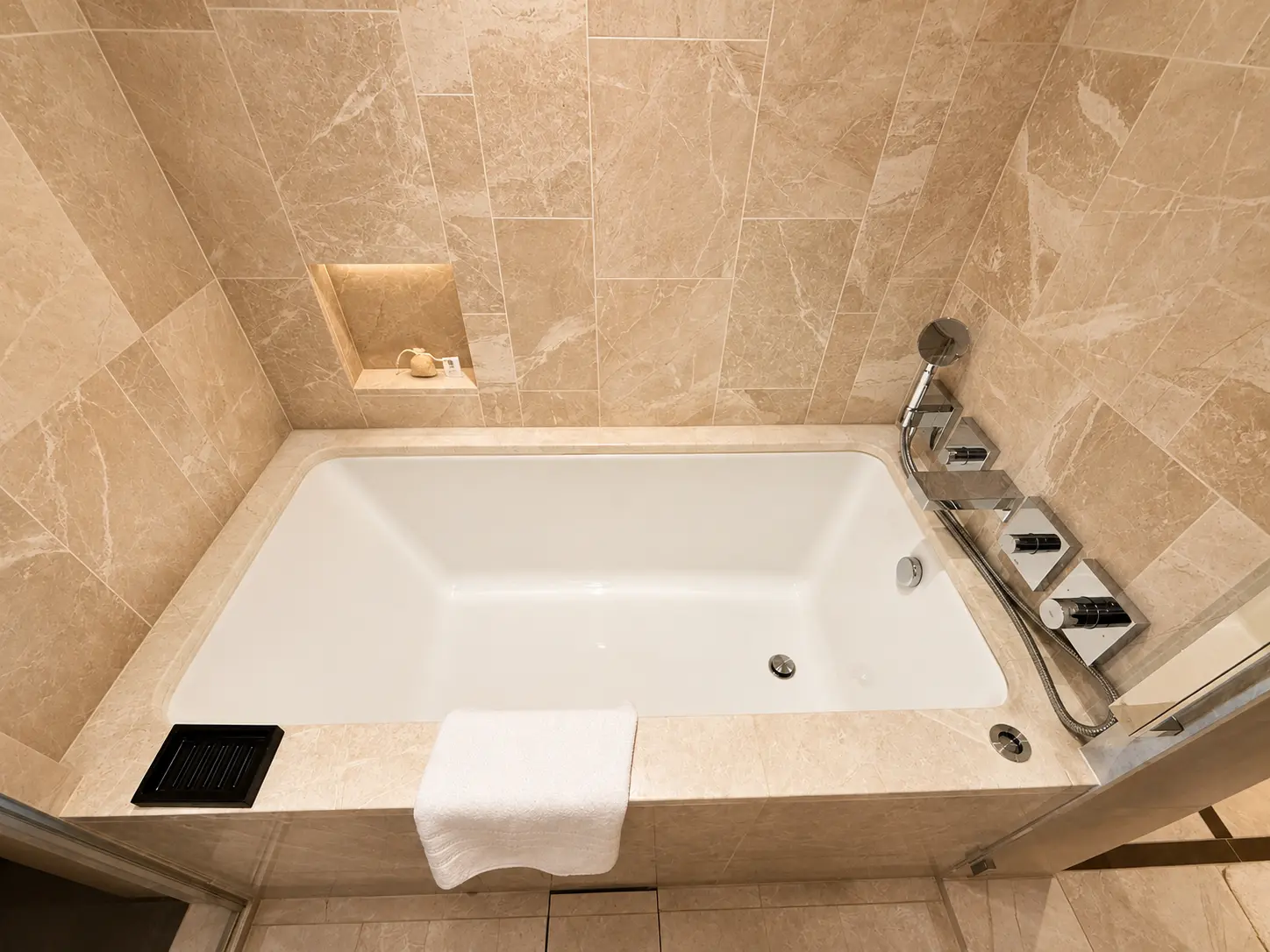Deep soaking bathtub surrounded by pale stone in a Deluxe Room at Four Seasons Hotel Kyoto.